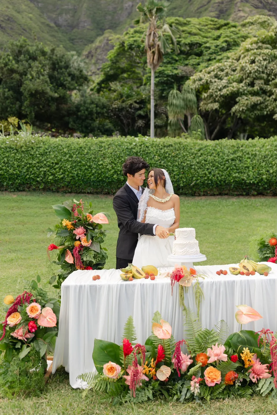 Newlyweds beside a white wedding cake and tropical floral table